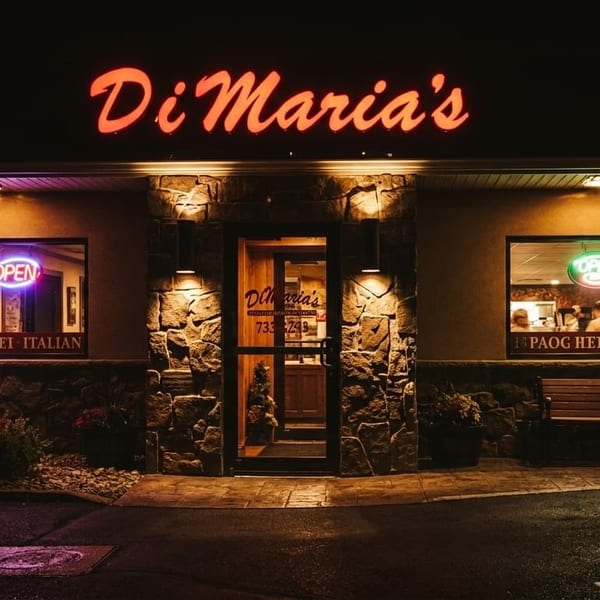 Di Maria's Italian restaurant exterior at night, with glowing red sign and neon 'OPEN' signs in windows.